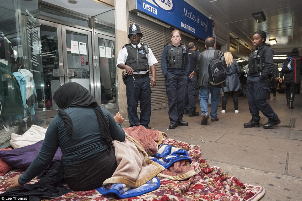 A woman who has been sleeping rough at Marble Arch smokes a cigarette as police and immigration officers talk to her during a major round-up operation in parts of London